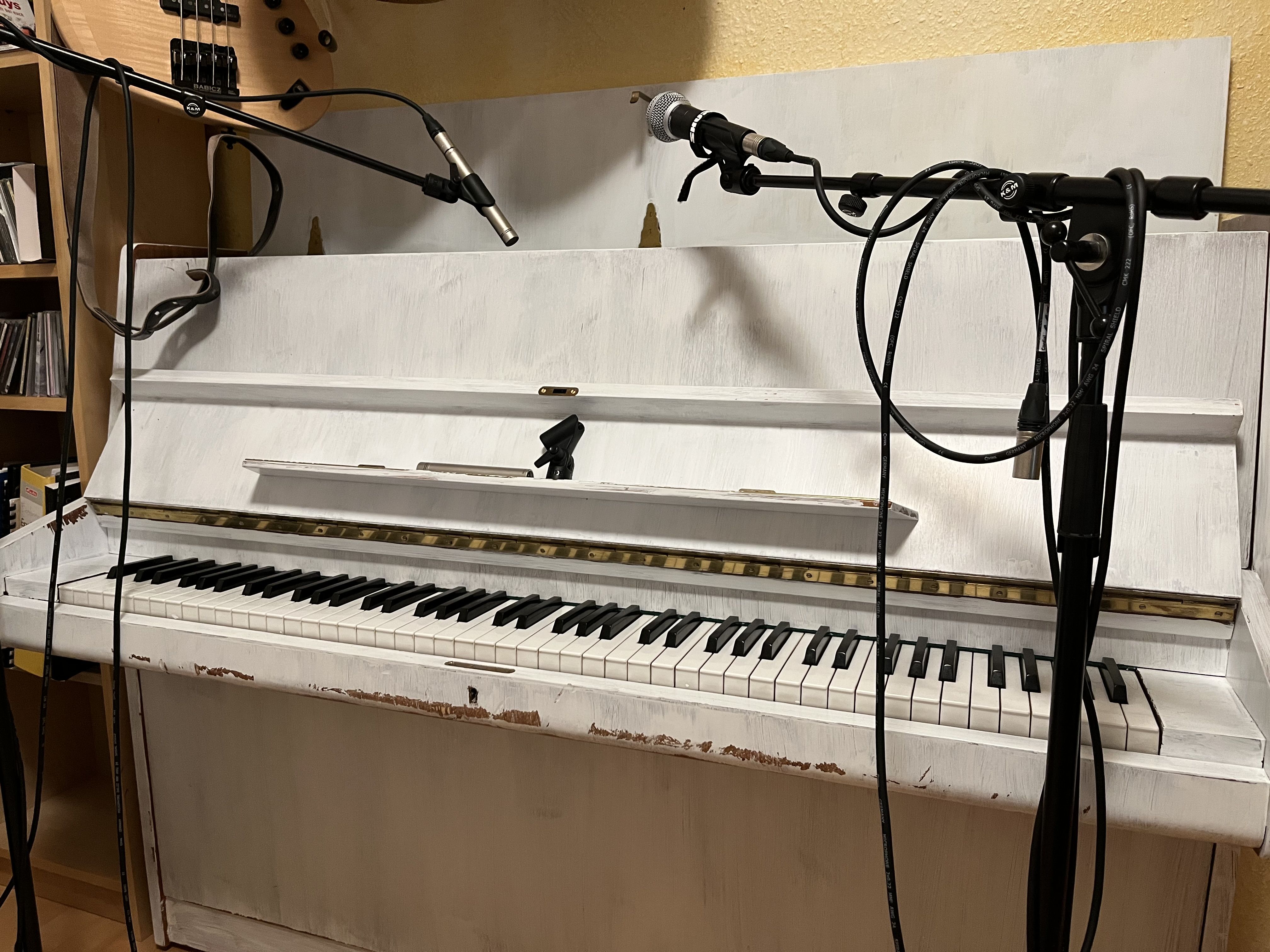 A white standup piano, equipped with two mircrophones for recording.
